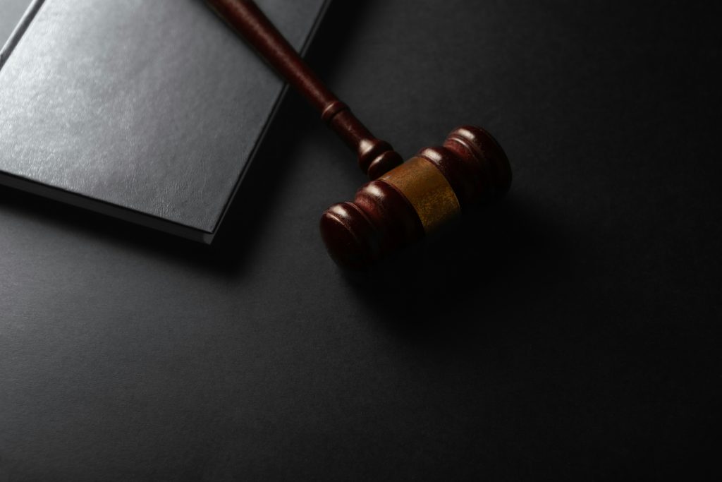 Wooden gavel resting on a dark surface next to book Wooden gavel resting on a dark surface next to book