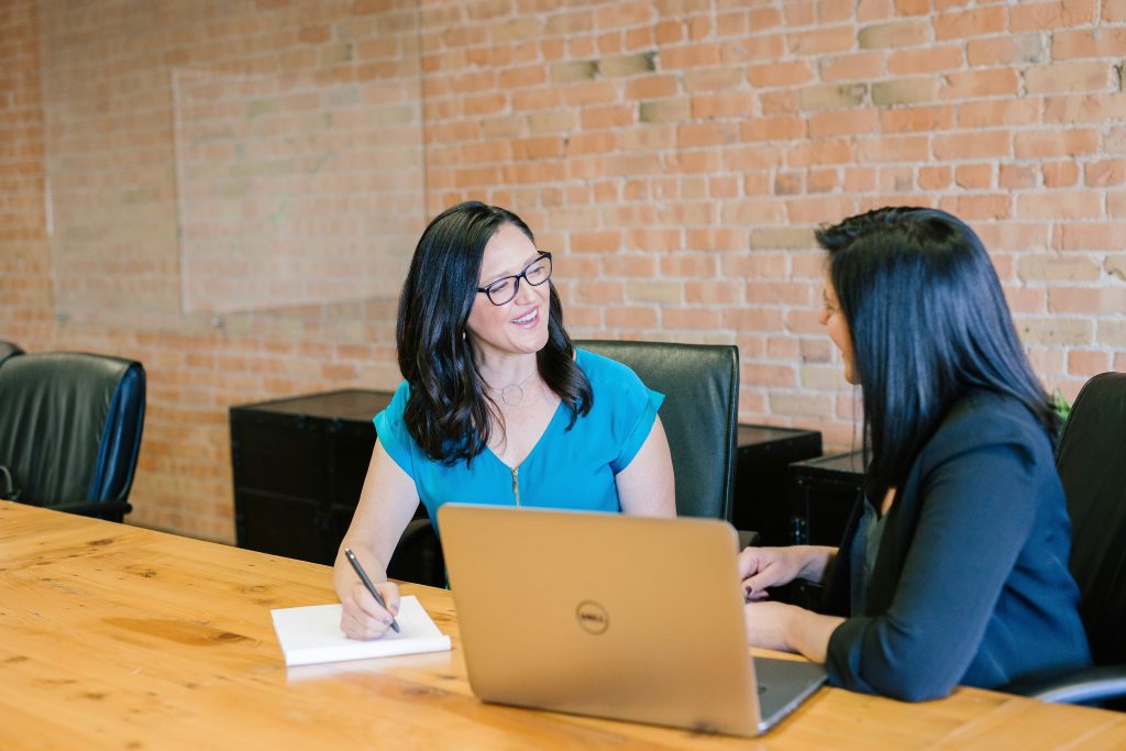 woman in teal t-shirt sitting beside woman in suit jacket woman in teal t-shirt sitting beside woman in suit jacket